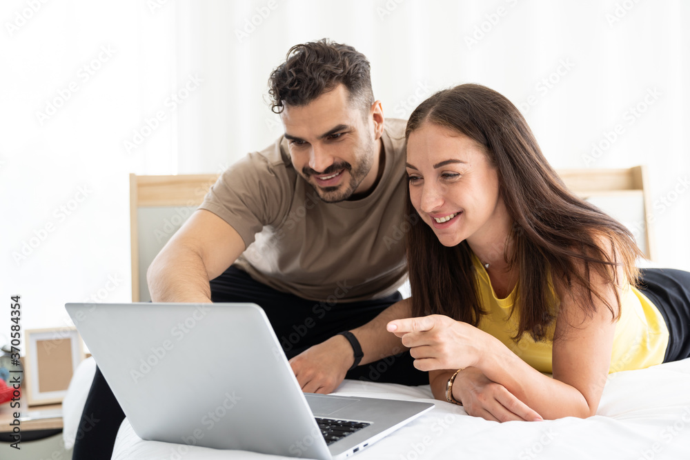 Young happy couple using laptop computer for video call or shopping online on the bed at home. Young happy couple using laptop computer for video call or shopping online on the bed at home.