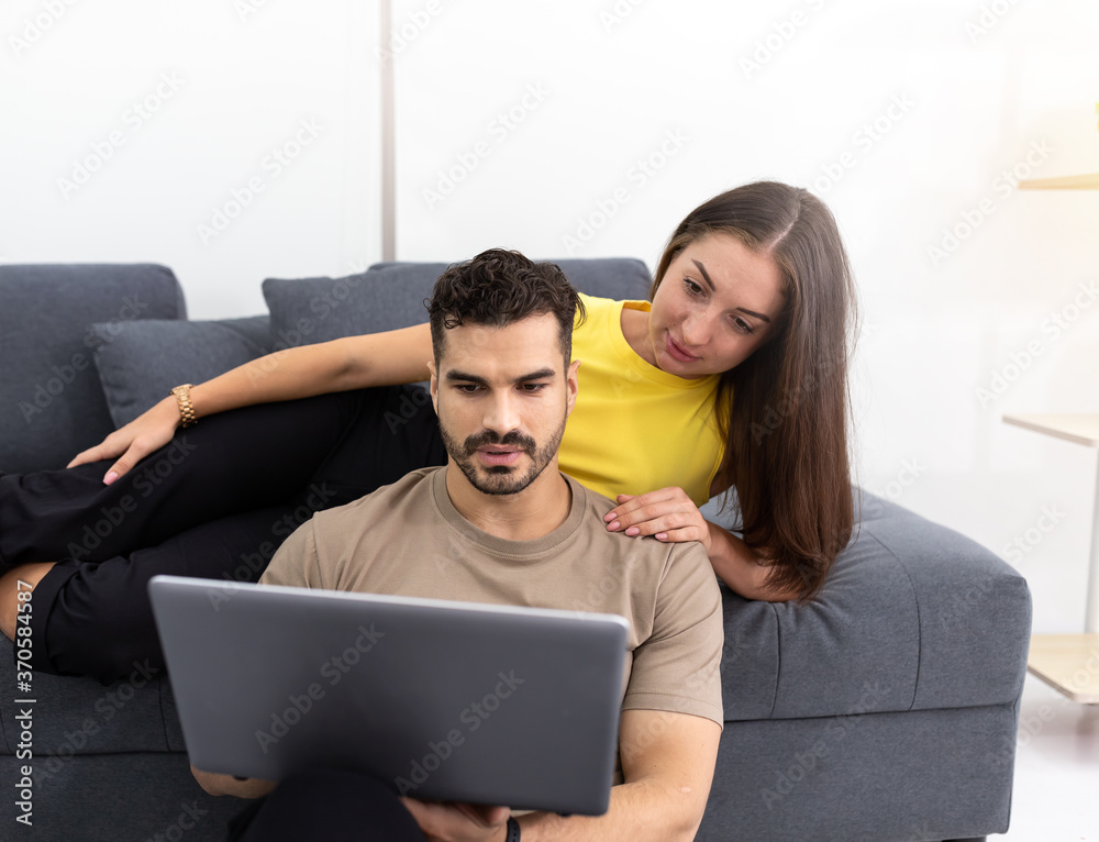 Young man and woman in casual outfit using laptop computer together in the living room at home. Creative businessman and woman work from home by video conference or shopping online during quarantined.