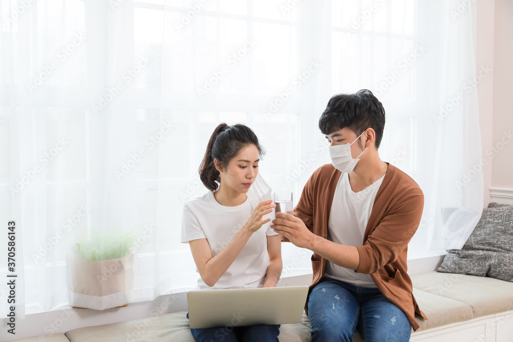 Couple wearing a protective face mask and woman working at home. But she got cold and flu, the man bringing her a hot drink and taking care of her. Couple wearing a protective face mask and woman working at home. But she got cold and flu, the man bringing her a hot drink and taking care of her.