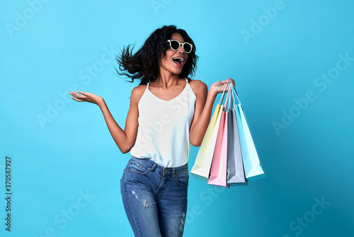 Canvastavla Portrait of an jovial beautiful woman holding shopping bags isolated on blue background