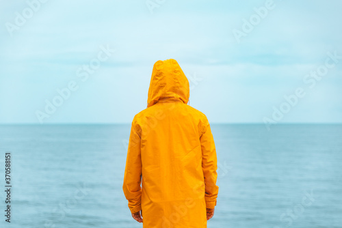 woman in yellow raincoat at sea beach cliff at storm rainy weather photo