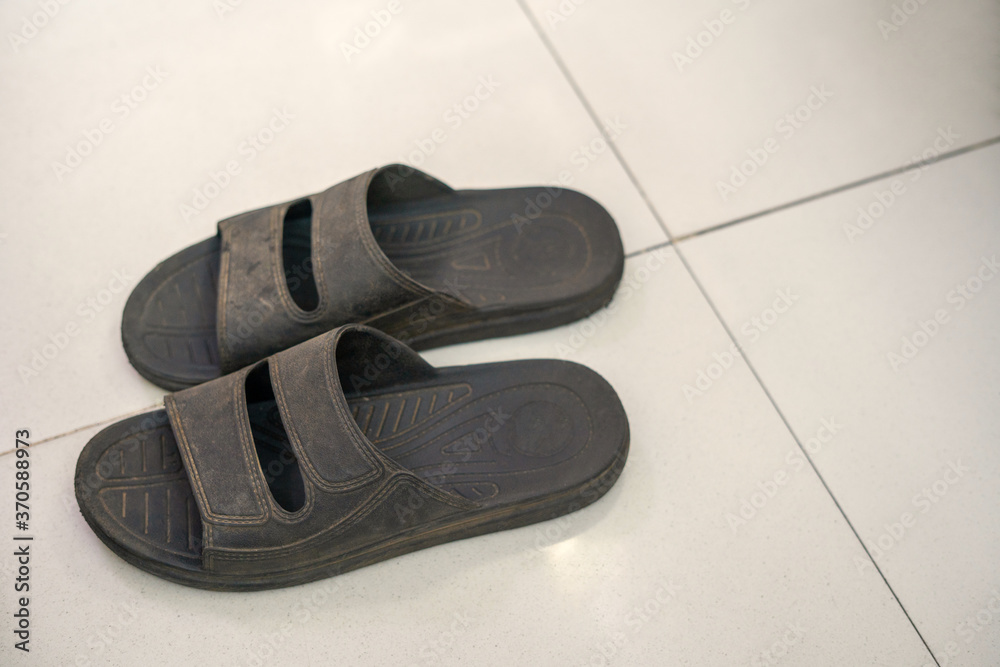 Black rubber shoes stained with mud on a cream-colored floor. Black rubber shoes stained with mud on a cream-colored floor.
