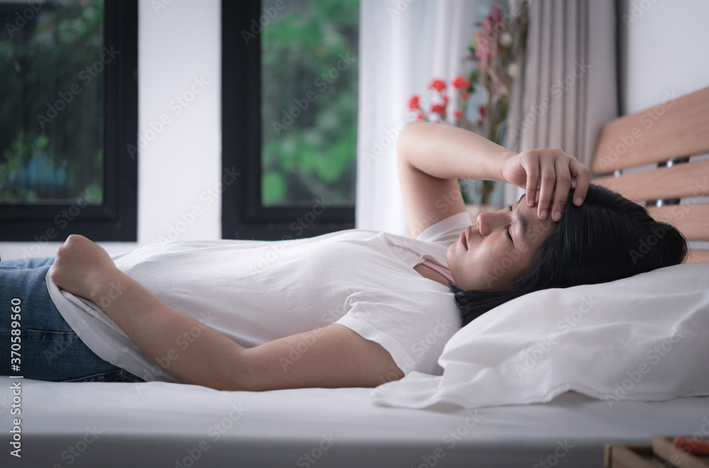 Beautiful woman in white t-shirt and blue jean get headache and cold lying down in bed to get better,healthy and medicine concept Beautiful woman in white t-shirt and blue jean get headache and cold lying down in bed to get better,healthy and medicine concept
