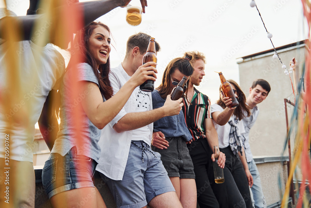 Fototapeta Leaning on the edge of the rooftop with decorates. Group of young people in casual clothes have a party together at daytime