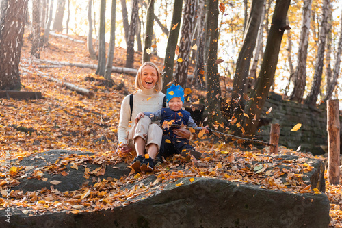 Boy and his mother are sitting in the autumn forest and tossing leaves.