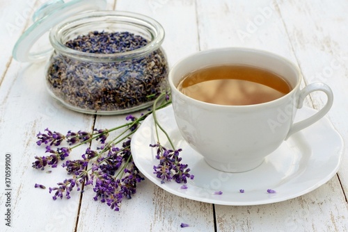 A Cup of tea with lavender flowers and a jar of dried lavender on a white wooden table close up