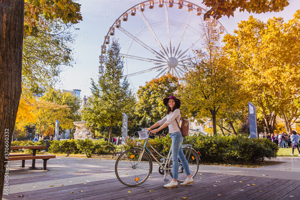 Fototapeta premium A happy young woman travel by bicycle and stop near the Budapest Eye big Ferris wheel in Budapest