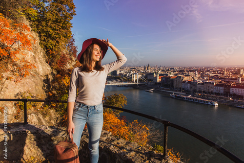 Photography A happy young woman enjoying her trip to Budapest, Hungary from the point from Gellert Hill during sunrise in autumn during sunrise