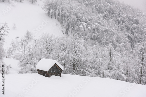 Minimalistic winter landscape with wooden house in snowy mountains. Cloudy weater, landscape photography