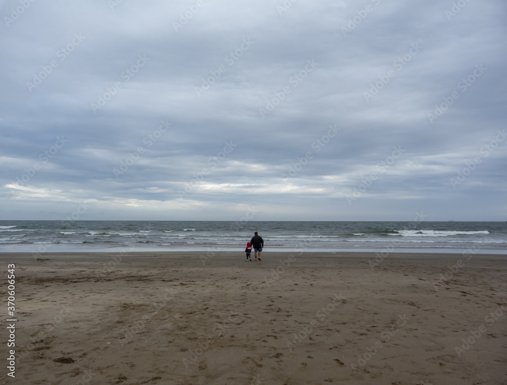Father and son, walking in the sand to the horizon (far)