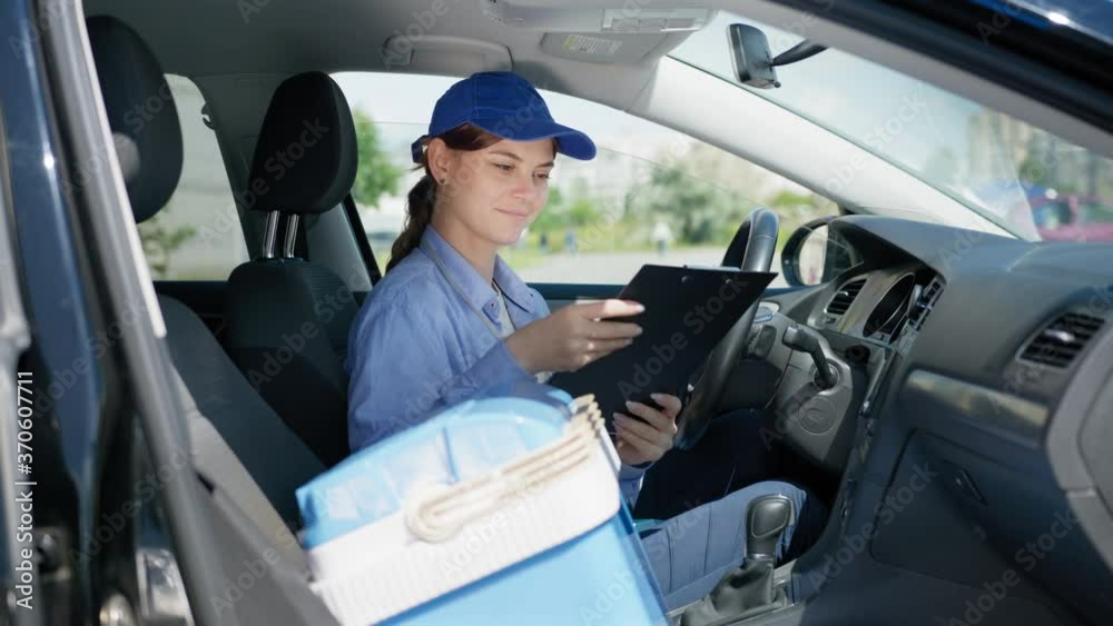 supermarket delivers, young attractive woman driver working as courier in food supply service of shop at home checks orders of customers while sitting in car supermarket delivers, young attractive woman driver working as courier in food supply service of shop at home checks orders of customers while sitting in car