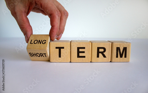 Hand turns a cubes and changes the expression 'SHORT TERM' to 'LONG TERM' or vice versa. Beautiful white background. Business concept, copy space. photo