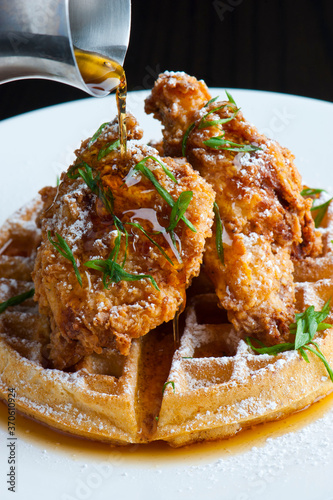 Chicken and waffles Classic American Diner Style Breakfast or Brunch menu item. Crispy homemade fried chicken on top of home buttermilk waffles topped with butter and maple syrup. 