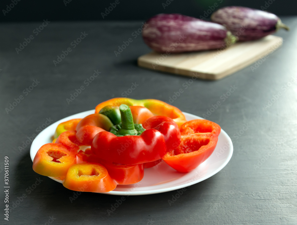 Colorful red peppers on a white plate.Gray background. eggplant on a wooden board Colorful red peppers on a white plate.Gray background. eggplant on a wooden board