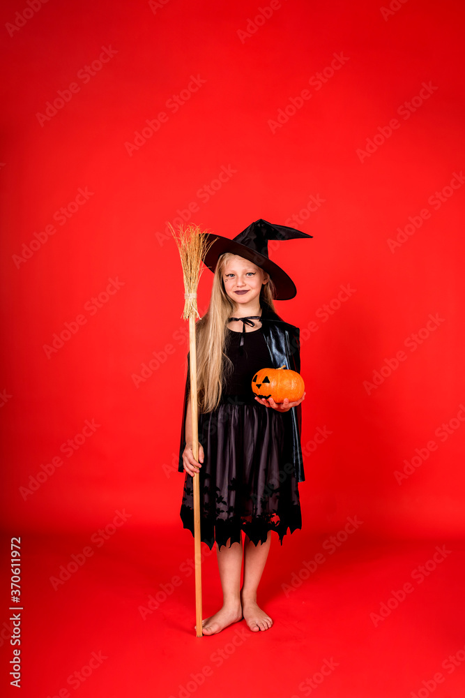 a beautiful full-length girl in a witch's costume with a hat with a broom and a pumpkin on Halloween on a red isolated background a beautiful full-length girl in a witch's costume with a hat with a broom and a pumpkin on Halloween on a red isolated background