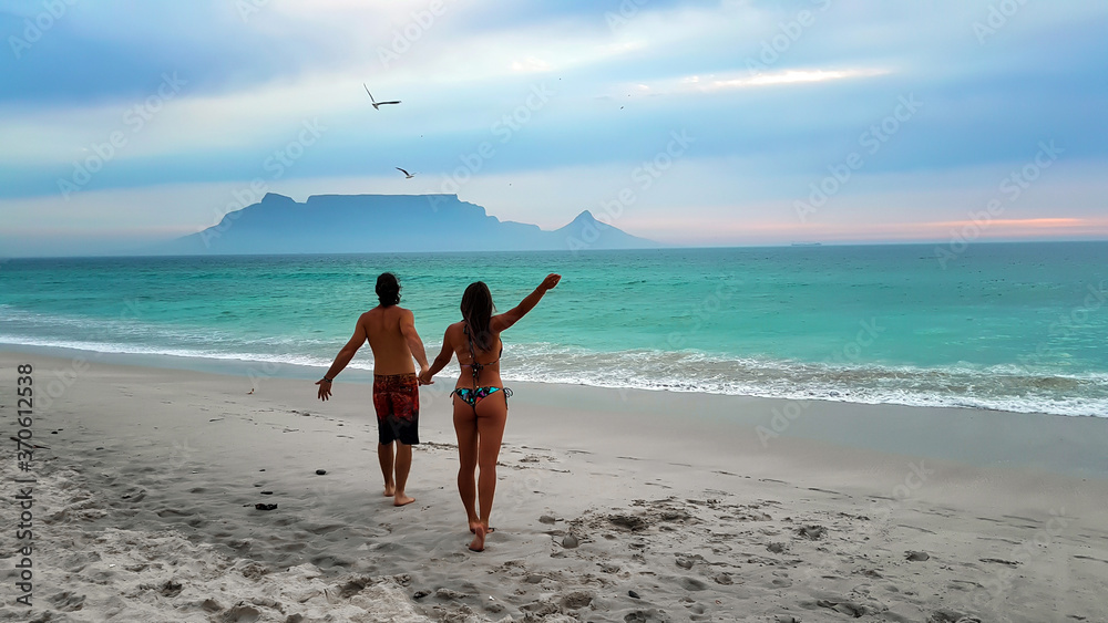 Obraz premium Young couple strolling on Cape Town beaches: Bloubergstrand and the view from Table Mountain