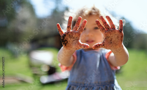 Small girl showing dirty hands outdoors in garden, sustainable lifestyle concept.