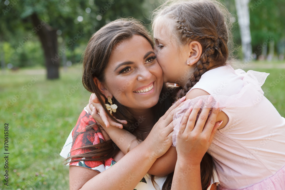 Naklejka premium Close up of a happy beautiful woman laughing while her daughter kissing her on a cheek outdoors