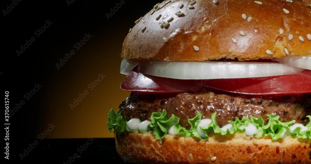 Delicious juicy burger rotating. Yummy hamburger with fresh onions, tomatoes, iceberg cabbage and grilled steak. Tasty pub grub close up shot 4k footage