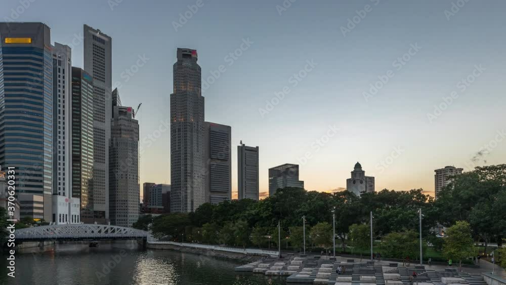 Singapore skyscrapers skyline with white Anderson Bridge and a few towers of financial district near esplanade park park day to night transition timelapse. Some green foliage on both sides. Singapore skyscrapers skyline with white Anderson Bridge and a few towers of financial district near esplanade park park day to night transition timelapse. Some green foliage on both sides.