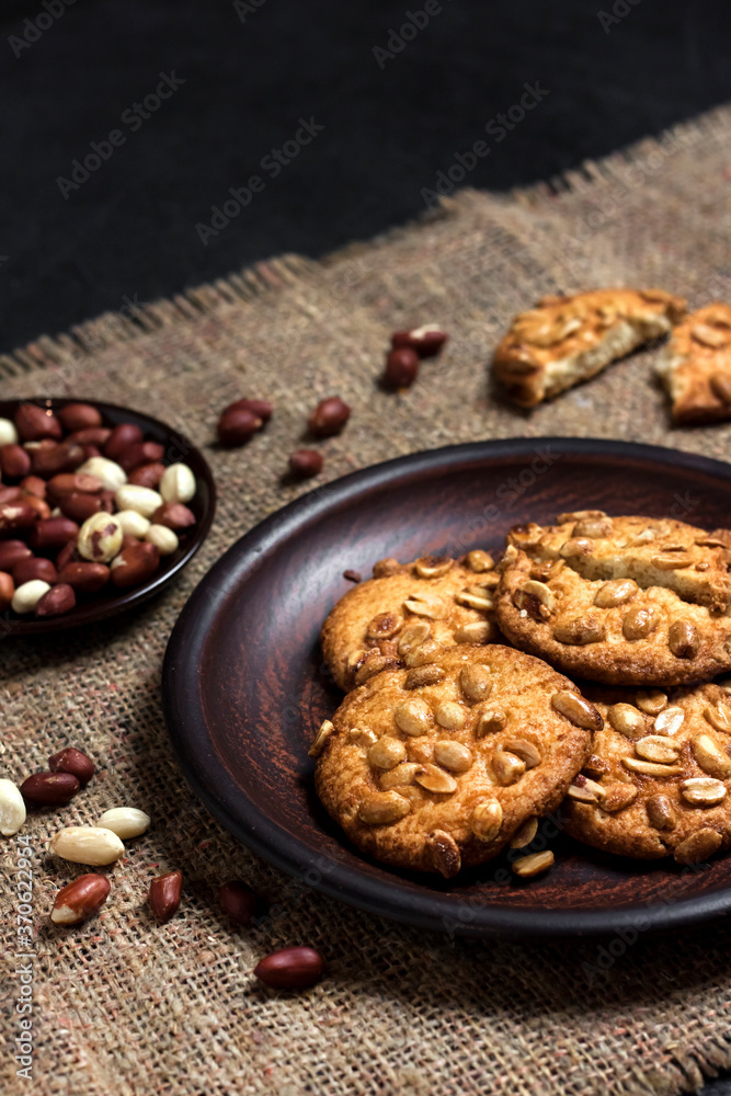 Homemade peanut cookies on a brown plate with raw peanuts in background Homemade peanut cookies on a brown plate with raw peanuts in background