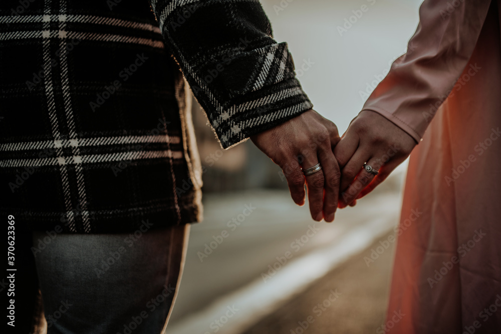 Interracial couple, man and woman holding hands, one wearing a gold wedding ring.