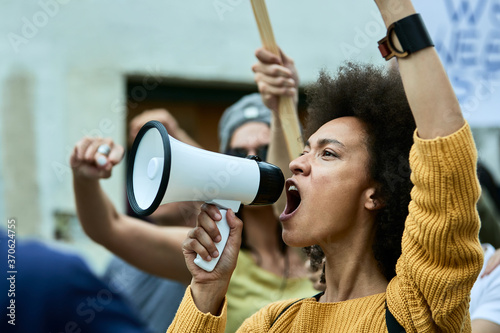 Fotografia African American woman with raised fist shouting through megaphone on anti-racism protest
