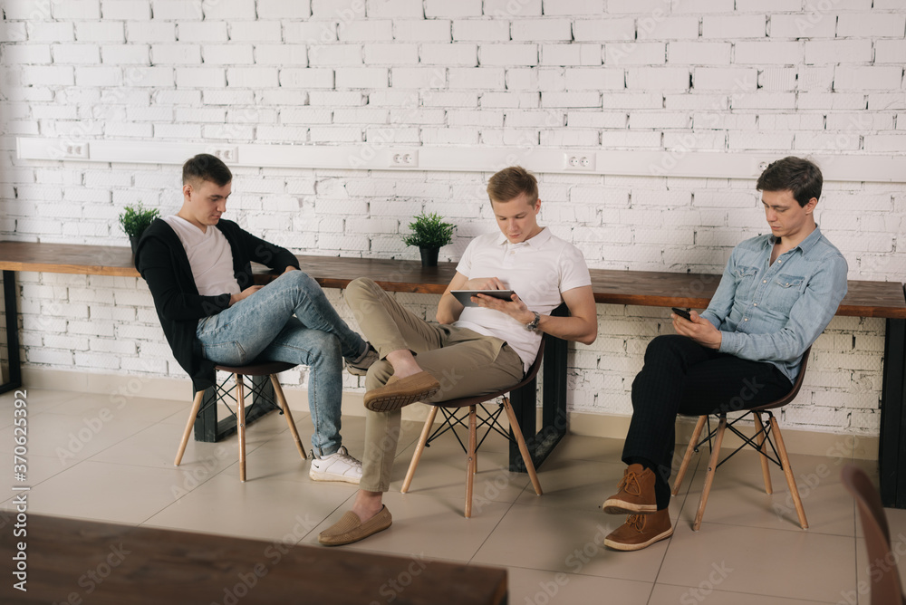 Group of young business people having break uses phone and tablet background of white brick wall. Concept of teamwork young business people. Group of young business people having break uses phone and tablet background of white brick wall. Concept of teamwork young business people.