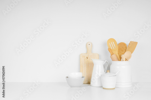 Kitchenware and utensils on a white shelf or counter against a white wall background with copy space. Home kitchen cooking decor.