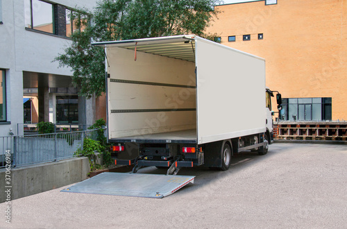 White delivery truck with tailgate open in front of an office building. Copy space. photo