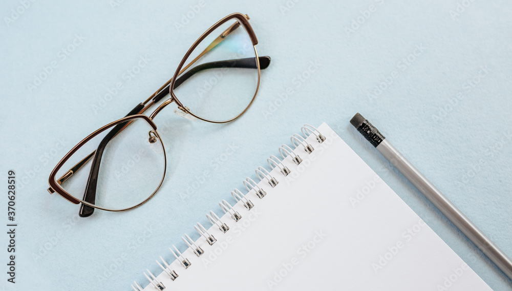 Office concept. Workspace with glasses, notebook and pencil. Copy space white and blue background. Office concept. Workspace with glasses, notebook and pencil. Copy space white and blue background.