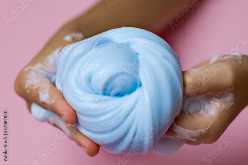  Blue slime toy in hands on a pink background.