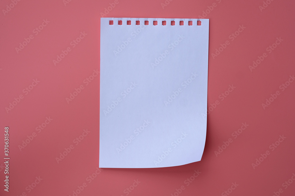 White sheet of notepad on a pink background. Blank paper sheet top view.