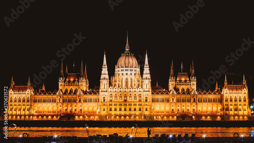 Panoramic background orange night image of Budapest parlament from the front side with boat and tourist taking a photo of the city. Travel in hungary and historical sites.
