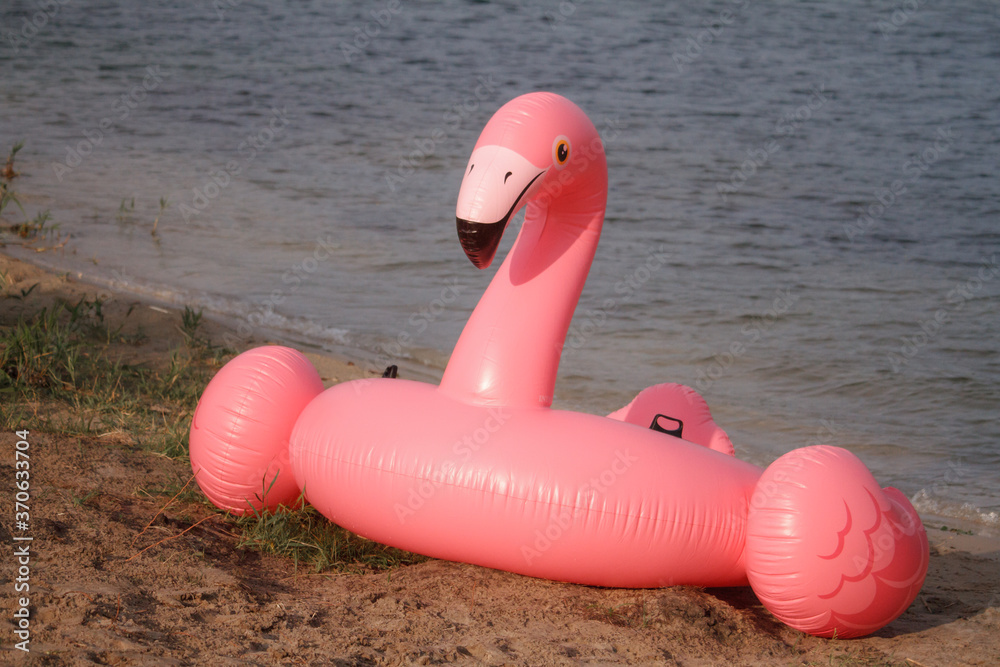 Giant inflatable pink flamingo float toy on sandy beach of river