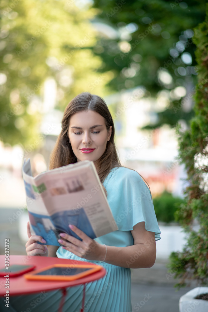 Fototapeta premium Charming brown-haired female reading sitting in cafe, reading newspaper
