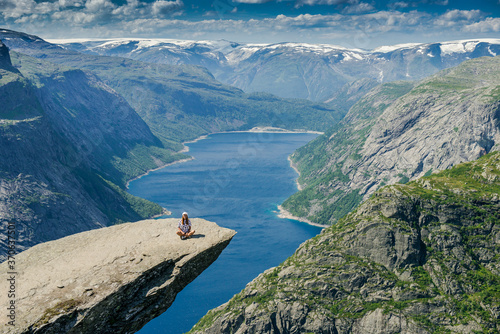 Girl sitting on the edge of a rocky cliff. Extreme tourism. Trolltunga. Troll language in Norway. Rocky ledge above the fjord. Natural landmark of Norway. 