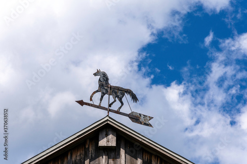 A vintage trotting horse whirligig weathervane twirls on the rooftop of an old barn.