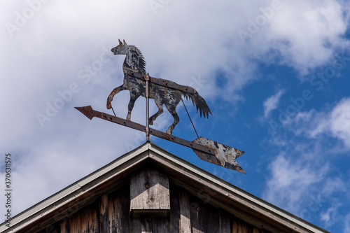 A vintage trotting horse whirligig weathervane twirls on the rooftop of an old barn. photo