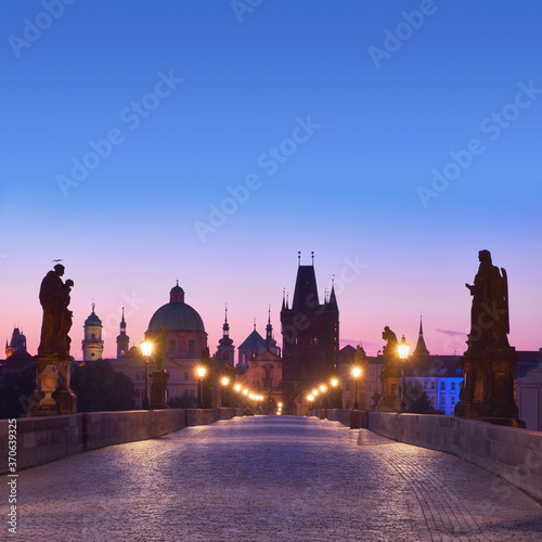 Charles Bridge at dawn, silhouette of Bridge Tower and saint sculptures with street lights in Prague, Czech Republic