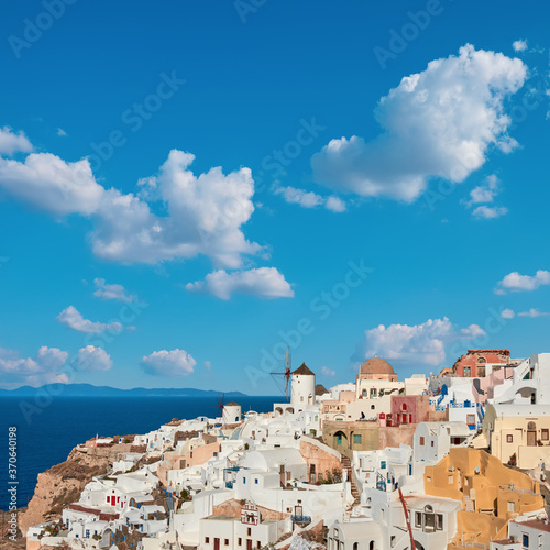 Windmills in Oia village, Santorini, Greece, under blue sky with clouds.