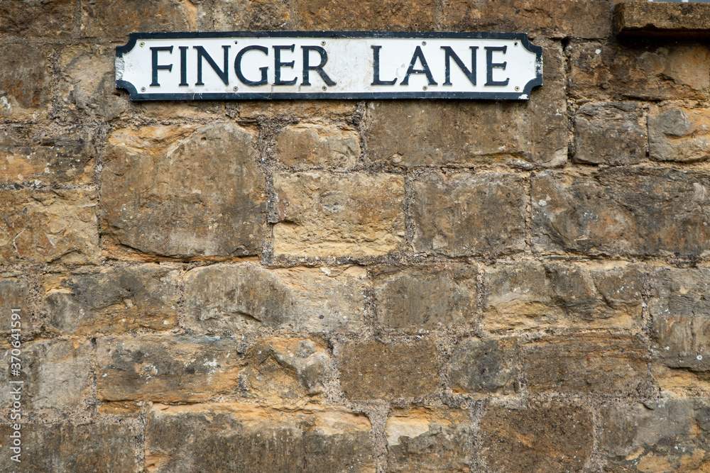 A street sign at the very top of the frame set against a brick stone wall.  The road sign says Finger Lane in traditional black on white UK town sign style.  Copy space available