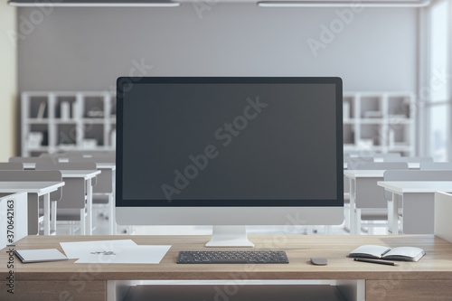 Black computer screen on table in luxury classroom interior.