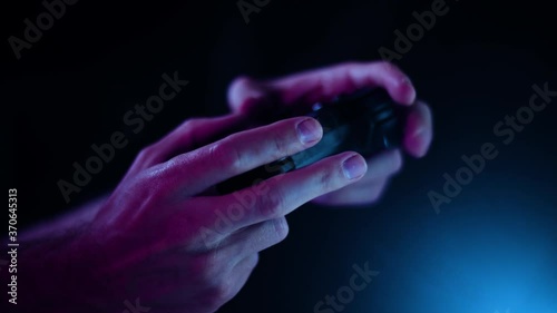 Playing video games in a darkened room with a black background close up on a small controller hands moving slowly blue lens flare