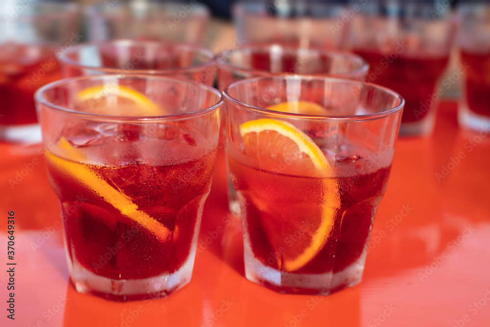View of alcohol setting on catering banquet table, row line of red colored aperitif alcohol cocktails on a party, negroni and spritz, vodka, and others on decorated catering bouquet table event View of alcohol setting on catering banquet table, row line of red colored aperitif alcohol cocktails on a party, negroni and spritz, vodka, and others on decorated catering bouquet table event