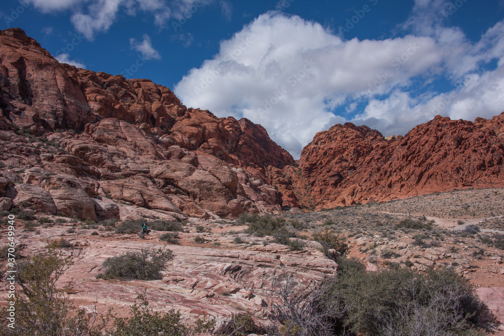 Red Rock Canyon  NCA, Nevada - March 2019: Aztec sandstone in red, pink and striped colors with mountain shaped cloud in blue sky.