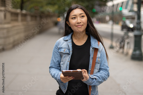 Young Asian woman walking street using tablet computer © blvdone