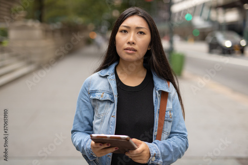 Young Asian woman walking street using tablet computer