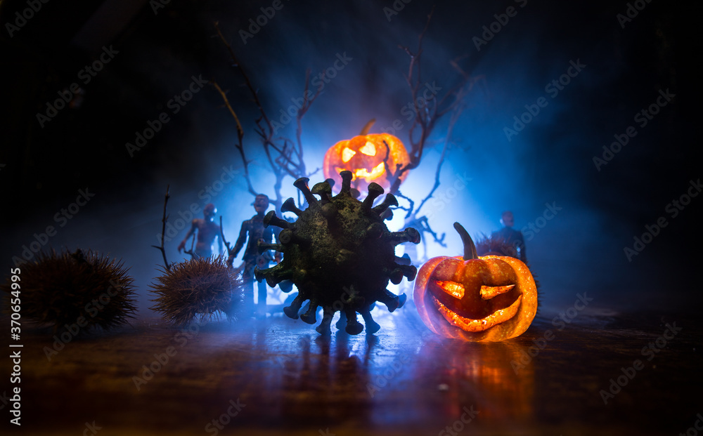 Halloween during Corona virus global pandemic concept. Glowing pumpkins and Covid novel on dark with thematic spooky decorations. Halloween pumpkin on foggy backlight.