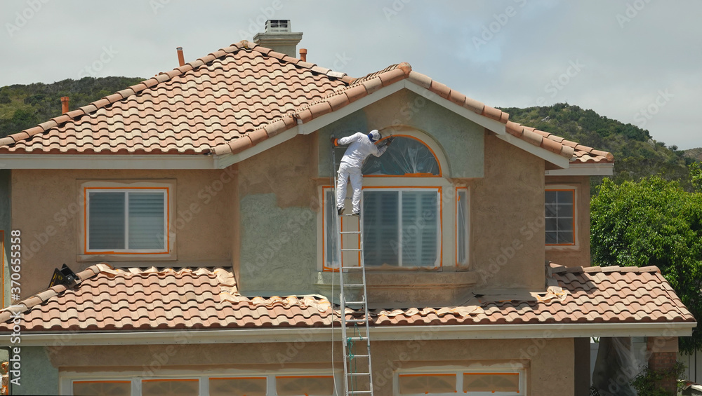 Worker leaning dangerously off the ladder to paint the stucco on a suburban home. Worker leaning dangerously off the ladder to paint the stucco on a suburban home.